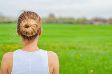 Beautiful young woman is practicing yoga on the grass. View of the back of a woman's head and...