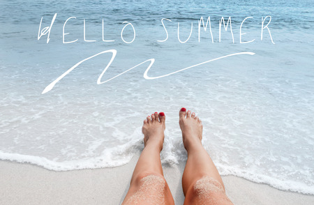 Sea background with lettering hello summer. Female legs on sandy beach. Vacation on the beachの写真素材