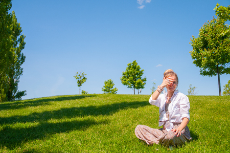 Happy woman is sitting on grass lawn. Beautiful boho style woman with accessories enjoying summer sunny day in park.の写真素材