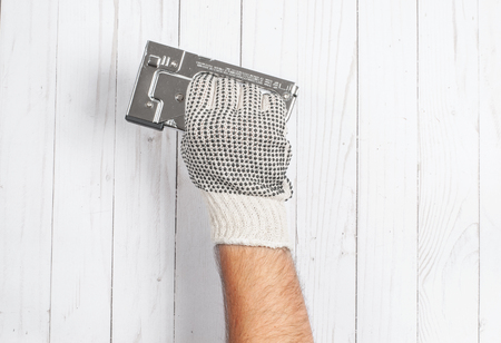Tool. Hand in glove is holding industrial stapler isolated on a white wooden background .の写真素材