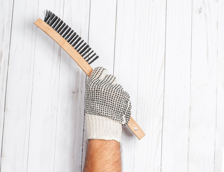 Tool. Hand in glove is holding wire metal brush isolated on a white wooden background .の写真素材