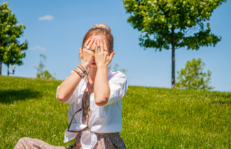 Beautiful boho style woman with accessories enjoy summer sunny day in park. Female hands with bracelets and rings is covering her face.の写真素材
