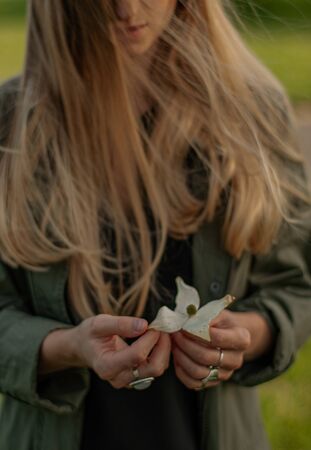 Beautiful woman with long hair holding flower in hand. Hands with rings stylish boho accessories. No focusの写真素材