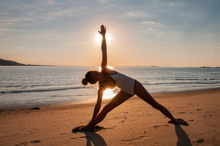 Silhouette of yoga woman on the beach at sunrise. Woman is practicing yoga at sunset on sea shore....