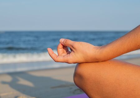 Close-up female hand in gyan mudra and lotus position. Woman practicing yoga and meditating on the beach.