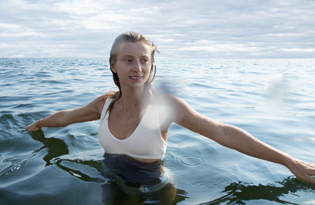 Relaxing on beach resort. Young beautiful woman enjoying seascape, standing in the water.