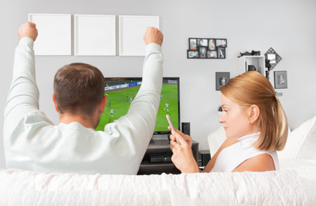 Happy man watching football on tv and woman looking at her smartphone