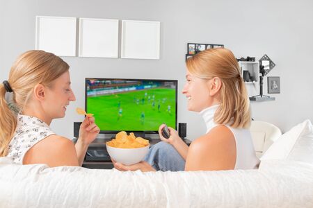 Happy friends or football fans watching soccer on tv sitting on couch at home.の写真素材