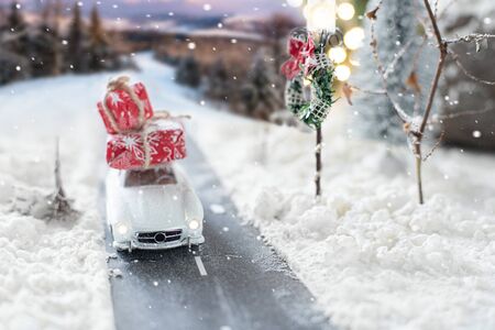 Miniature classic car carrying a christmas gifts on snowy winter landscapeの写真素材