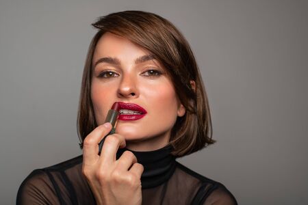 Professional Makeup. Beautiful brunette woman is applying lipstick. Perfect make up with red lipsの写真素材