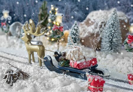 Sled loaded of gifts and miniature car carrying a christmas tree on snowy winter backgroundの写真素材