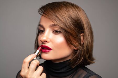 Professional Makeup. Beautiful brunette woman is applying lipstick. Perfect make up with red lipsの写真素材