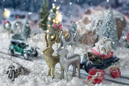 Sled loaded of gifts and miniature car carrying a christmas tree on snowy winter backgroundの写真素材