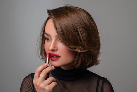 Professional Makeup. Beautiful brunette woman is applying lipstick. Perfect make up with red lipsの写真素材