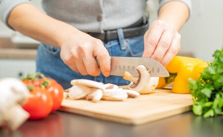 Woman is cutting mushroom on kitchen table. Fresh vegetables for cookingの写真素材