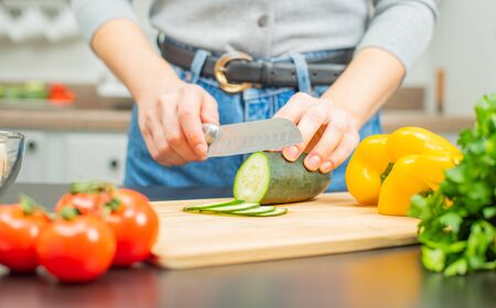 Woman is cutting cucumber on cut board on kitchen. Fresh vegetables for saladの写真素材