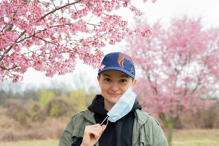 Beautiful woman takes off a medical mask and enjoying blooming tree after allergyの写真素材