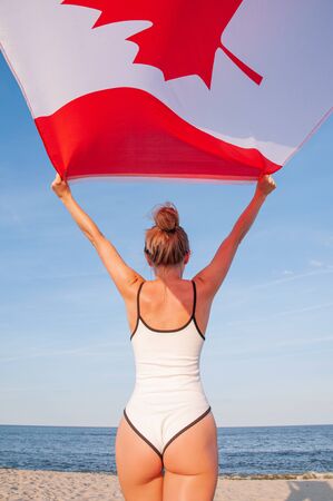 National Flag of Canada. Beautiful patriotic woman holding canadian flag on the beach.の写真素材