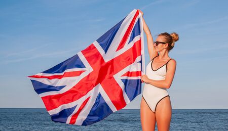 National Flag of United kingdom. Beautiful patriotic woman holding british flag on the beach.の写真素材