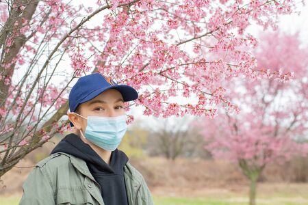 Beginning of Spring. Young woman in protective mask from pollen allergy, among blooming trees in park.の写真素材