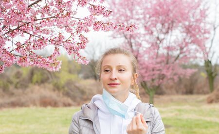 Beautiful woman takes off a medical mask and enjoying blooming tree after allergyの写真素材
