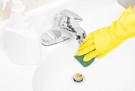 Woman in yellow rubber gloves is cleaning bathroom sink with detergent and spongeの写真素材