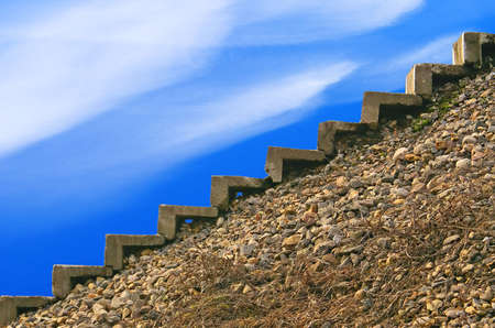 Steps of an old ladder on an abrupt stony slope, the bright dark blue sky, light easy plumose clouds. の写真素材