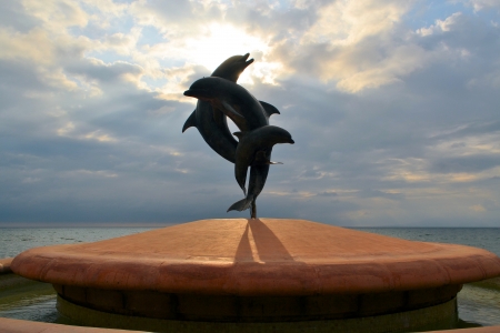 statue of couple jumping dolphins, blue sea and sky, clouds, sunの写真素材