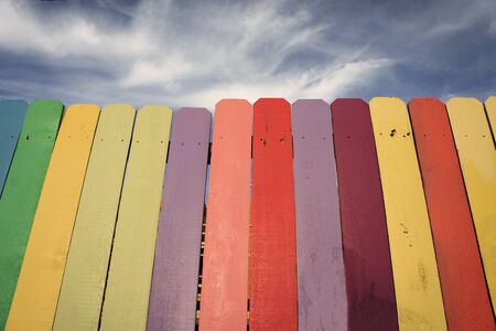 Wooden fence painted in the colors of the rainbow with blue skyの写真素材