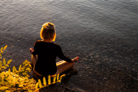 A woman does yoga by a lake at sunset. The weather is warm and the lake is calm. The mood is relaxed. The woman is athletic. It's autumn.の写真素材