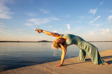 A woman does yoga by a lake at sunset. The weather is warm and the lake is calm. The mood is relaxed. The woman is athletic. It's autumn.の写真素材