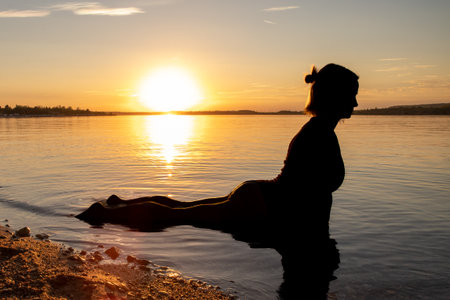 A woman does yoga by a lake at sunset. The weather is warm and the lake is calm. The mood is relaxed. The woman is athletic. It's autumn.の写真素材