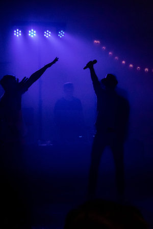 Party mood at a concert. It is dark. The party light is blue. People are seen in silhouette.