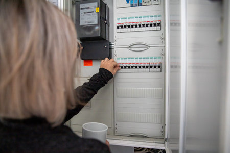 A woman is standing at the fuse box. The aim is to reduce power consumption and save electricity. It...