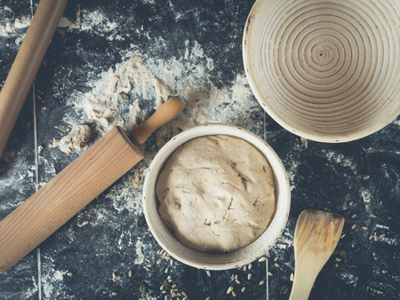 topview of dark kitchen table decorated with a lot of flour, pumpkin seeds, sourdough in wooden bannetons, rolling pin,の写真素材