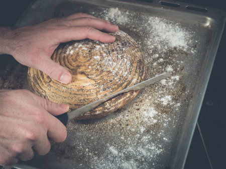 image shows a hand holding a homemade loaf of bread while cutting the bread into slices; situation...