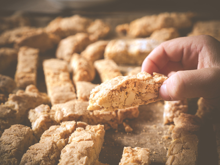 photo shows a jung hand  demonstrating a homemade crunchy biscotti; with more biscotti and baking sheed in the backgroundの写真素材