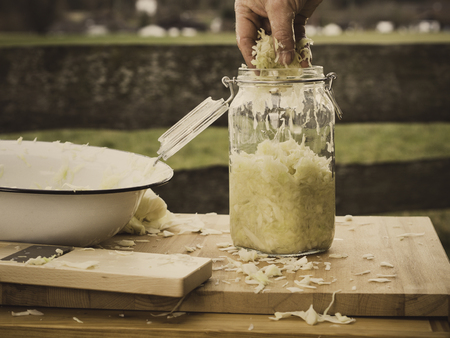 image shows how to make easy homemade sauerkraut in a mason jar - hand is filling the glass with sliced cabbageの写真素材