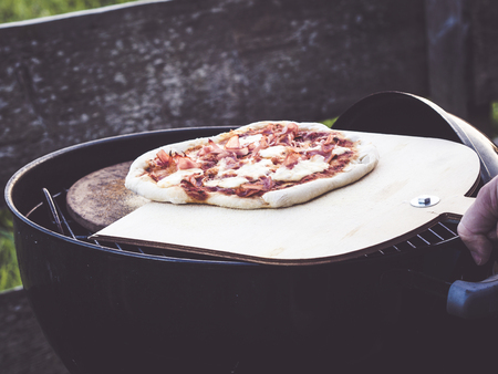 image shows a homemade crunchy grilled pizza; hand holding pizza shovel with fresh handmade pizzaの写真素材
