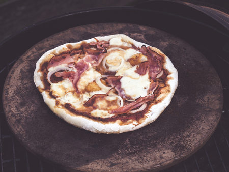 top view of homemade grilled pizza on a pizza stone with cheese, ham, tomato sauceの写真素材