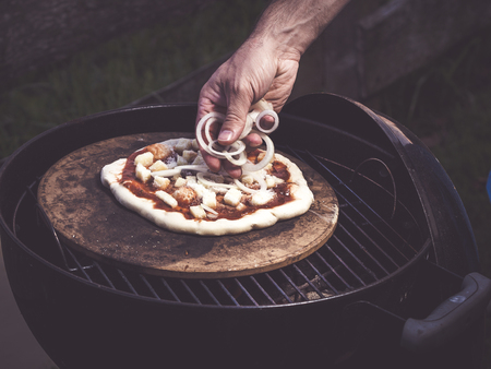 preparing best homemade grilled pizza ever adding toppings like onionsの写真素材