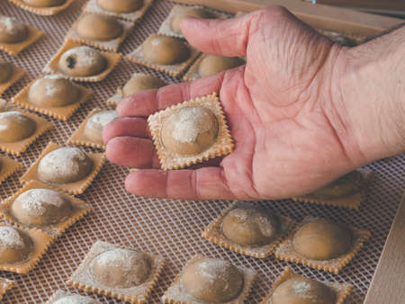 image shows hand with fresh homemade ravioli or pasta close to pasta squares,ravioli or tortellini during drying processの写真素材