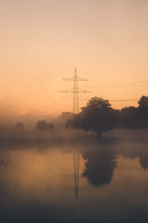 Powerline on hazy morning with reflection in lake