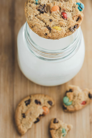 Glass of milk and homemade sugar cookies with colorful chocolate candies on a wooden board. Copy...