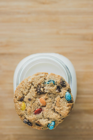 Glass of milk and homemade sugar cookies with colorful chocolate candies on a wooden board. Copy...