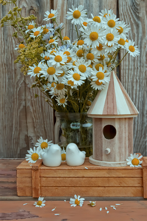 Summer composition. Porcelain birds, a birdhouse and a bouquet of chamomiles, against a wooden wall. Stylish still life for the production of postcards, posters, etc.の写真素材