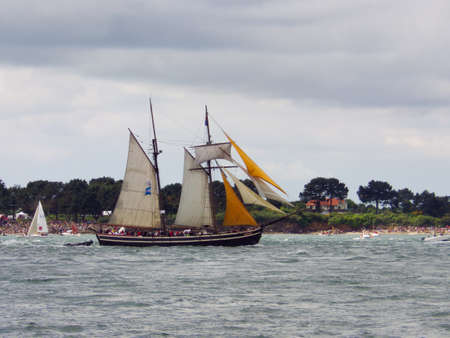 The historic Etoile de France sailboat sails on the ocean surrounded by small boats, the Breton coast is visible.のeditorial素材