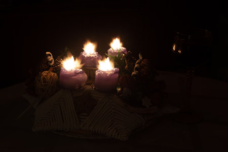 An Advent wreath with its four lighted candles, a stemmed glass is placed next to it.の写真素材