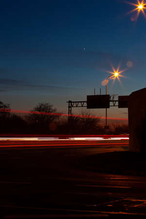 A star shines in the night sky. Red streaks of lights indicate the speed of the carsの写真素材