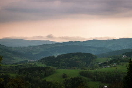 The weather is overcast, the vegetation is very green. The mountains ripple under the dark clouds with a touch of pink clouds also.の写真素材
